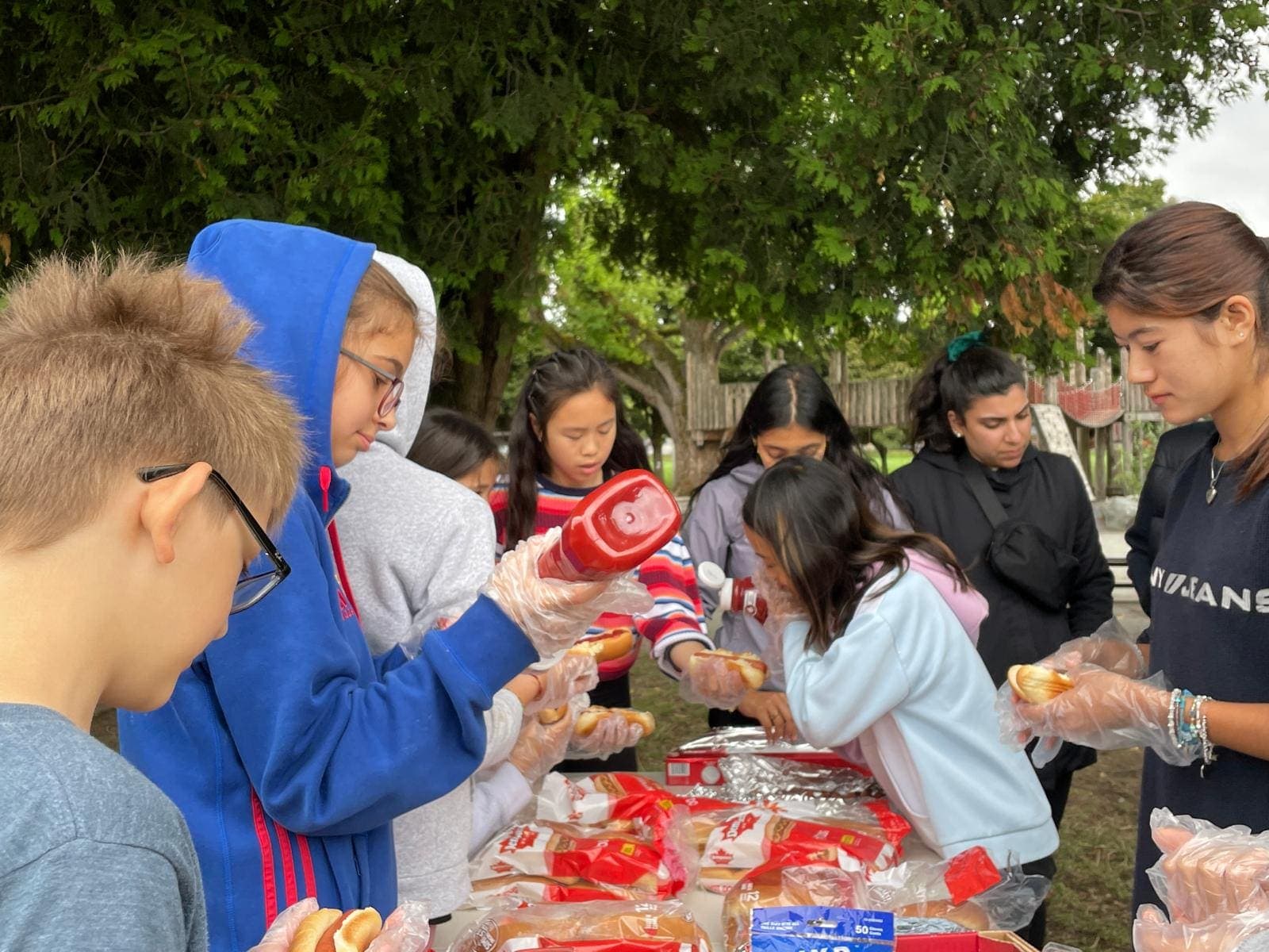 Junior youth serving food they prepared together at an outdoor community event.